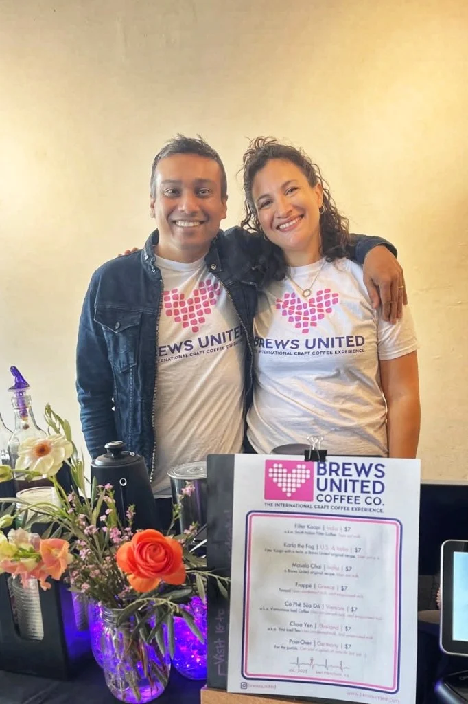 Danielle and Azmath, founders of Brews United Coffee Co., behind the cart in Brews United T-shirts, the menu board in front of them